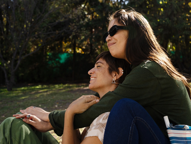 A happy lesbian couple hold each other while enjoying the sun outside at a park.