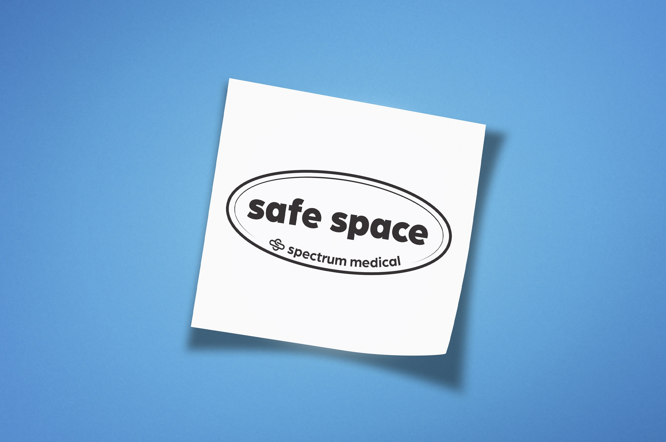 A clean white sticker with the words "safe space" in bold, surrounded by an oval outline, is placed against a bright blue background. Below the text, the "Spectrum Medical" logo is subtly included, emphasizing inclusivity and support. The minimalist design conveys a clear and welcoming message.