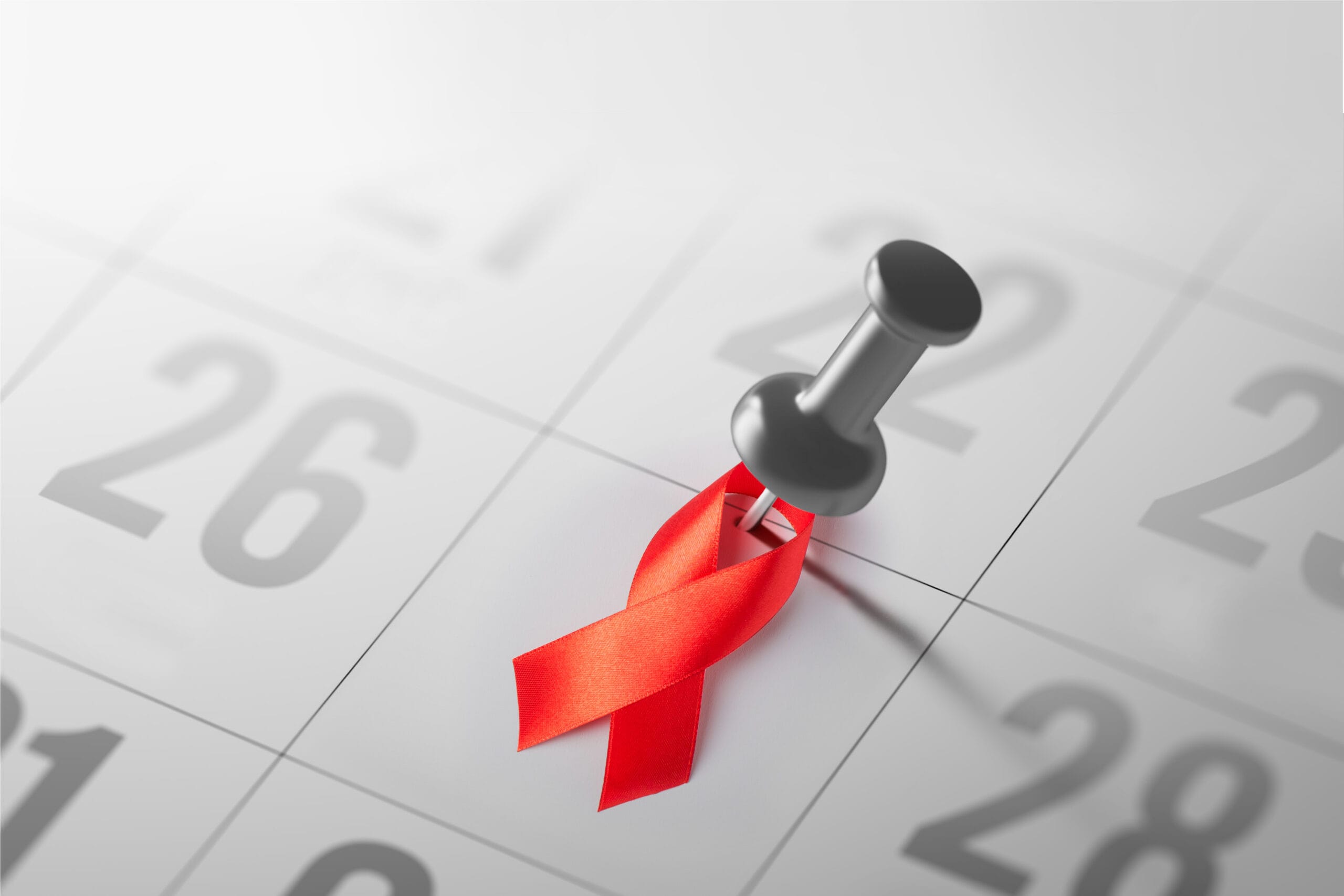 A red ribbon, the symbol of World AIDS Day, pinned to a calendar on the date December 1st.