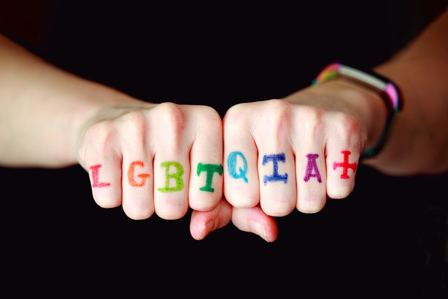 Two hands with the letters "LGBTQIA+" written on the knuckles in rainbow colors, representing the LGBTQIA2S+ community.