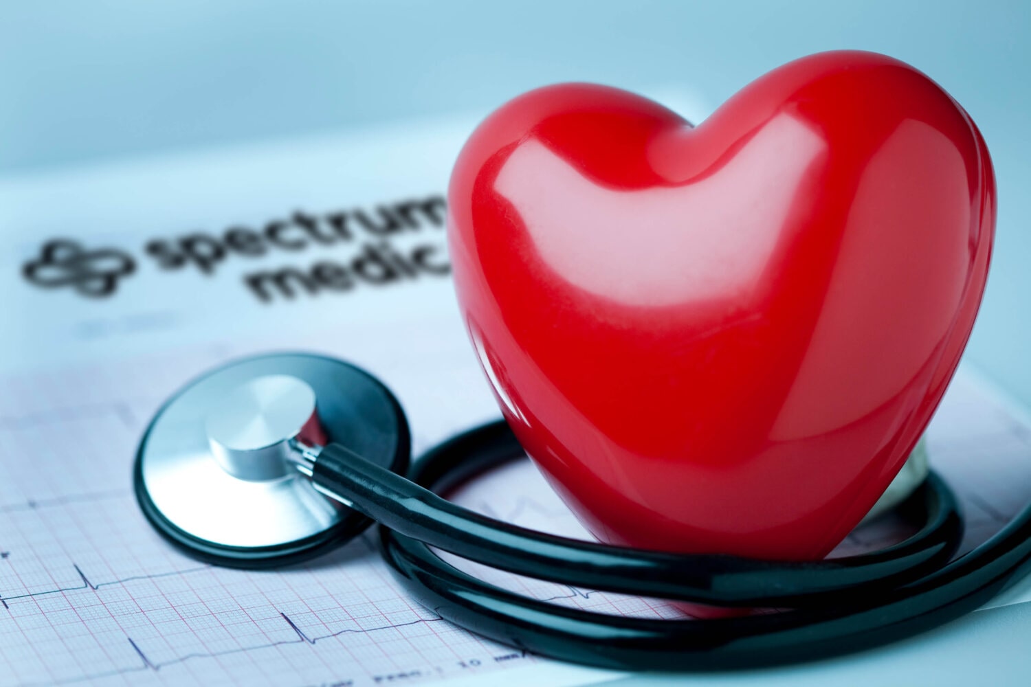 A red heart-shaped object resting on a medical chart with a stethoscope draped over it. The chart appears to have an EKG reading. This image may represent heart health or cardiology services.