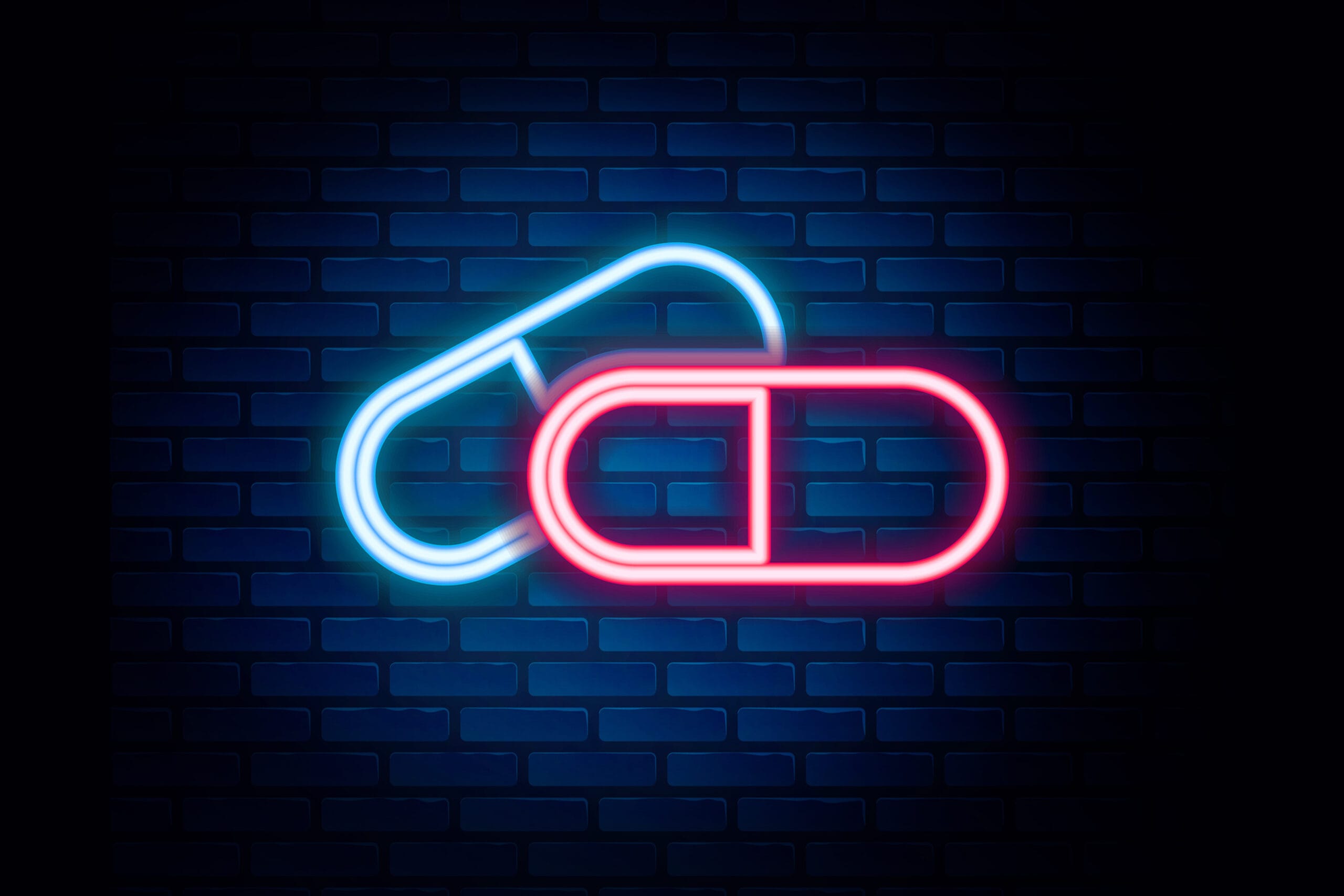 Two neon signs of pills, one blue and one red, overlapping each othTwo neon signs of pills, one blue and one red, overlapping each other on a brick wall background. This image is likely used to represent medication or a pharmacy.er on a brick wall background.