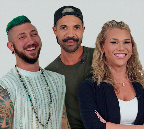 A group of three smiling individuals stands together against a plain white background. On the left, a person with green hair, tattoos, and piercings wears a striped top and layered necklaces. In the middle, a person with a mustache, wearing a green shirt and a backward cap. On the right, a person with long blonde hair and a bright smile wears a dark cardigan over a white top. The image radiates positivity and individuality.