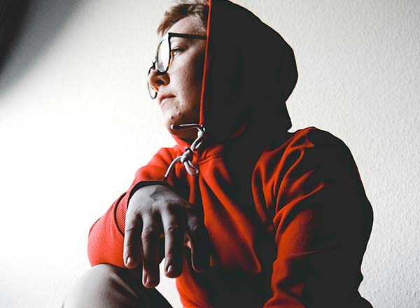 Thoughtful person in a red hoodie looking out a window, symbolizing reflection on red flags and emotional well-being in LGBTQ+ relationships.