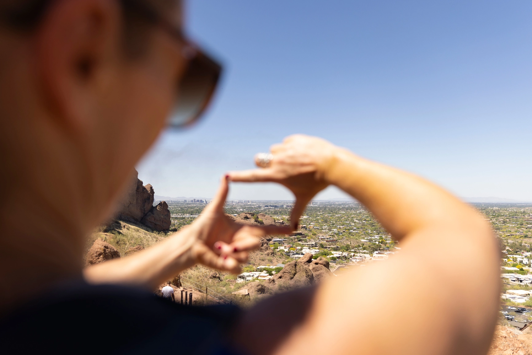 A person looking down at the city of Phoenix from a vantage point uses their fingers to make a view finder box out over the Phoenix horizon.