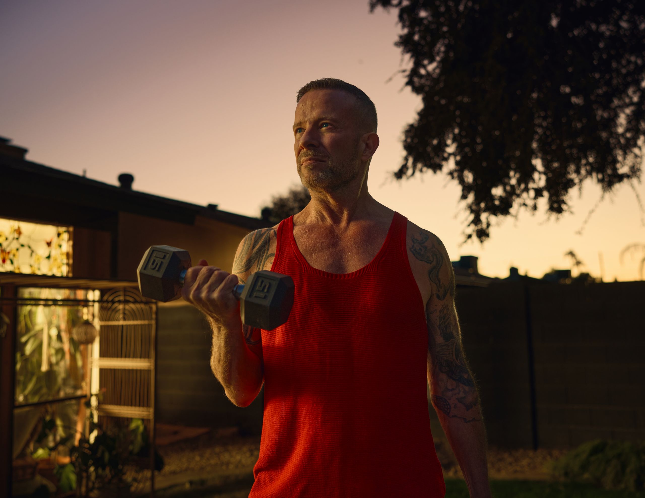 Person exercising outdoors at sunset while lifting a dumbbell, representing strength, wellness, and healthy living.