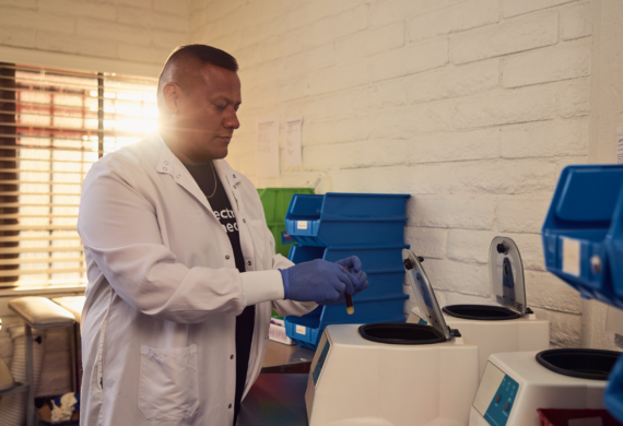 Spectrum Medical laboratory professional wearing a white lab coat and gloves prepares a blood sample for testing in the clinic’s laboratory.