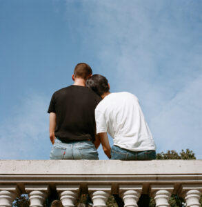 two partners sit with their backs to us, looking up towards a blue sky