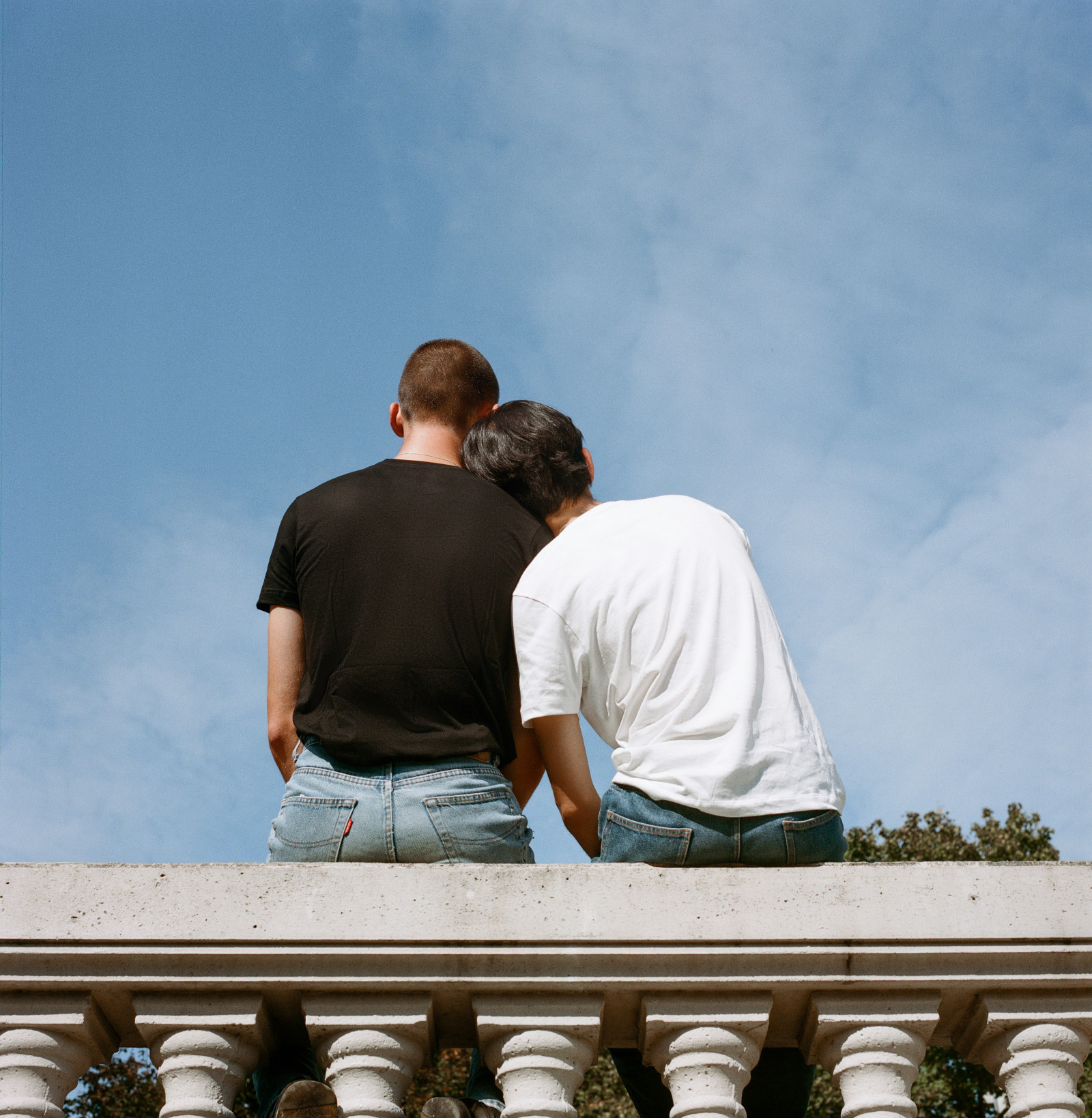 two partners sit with their backs to us, looking up towards a blue sky