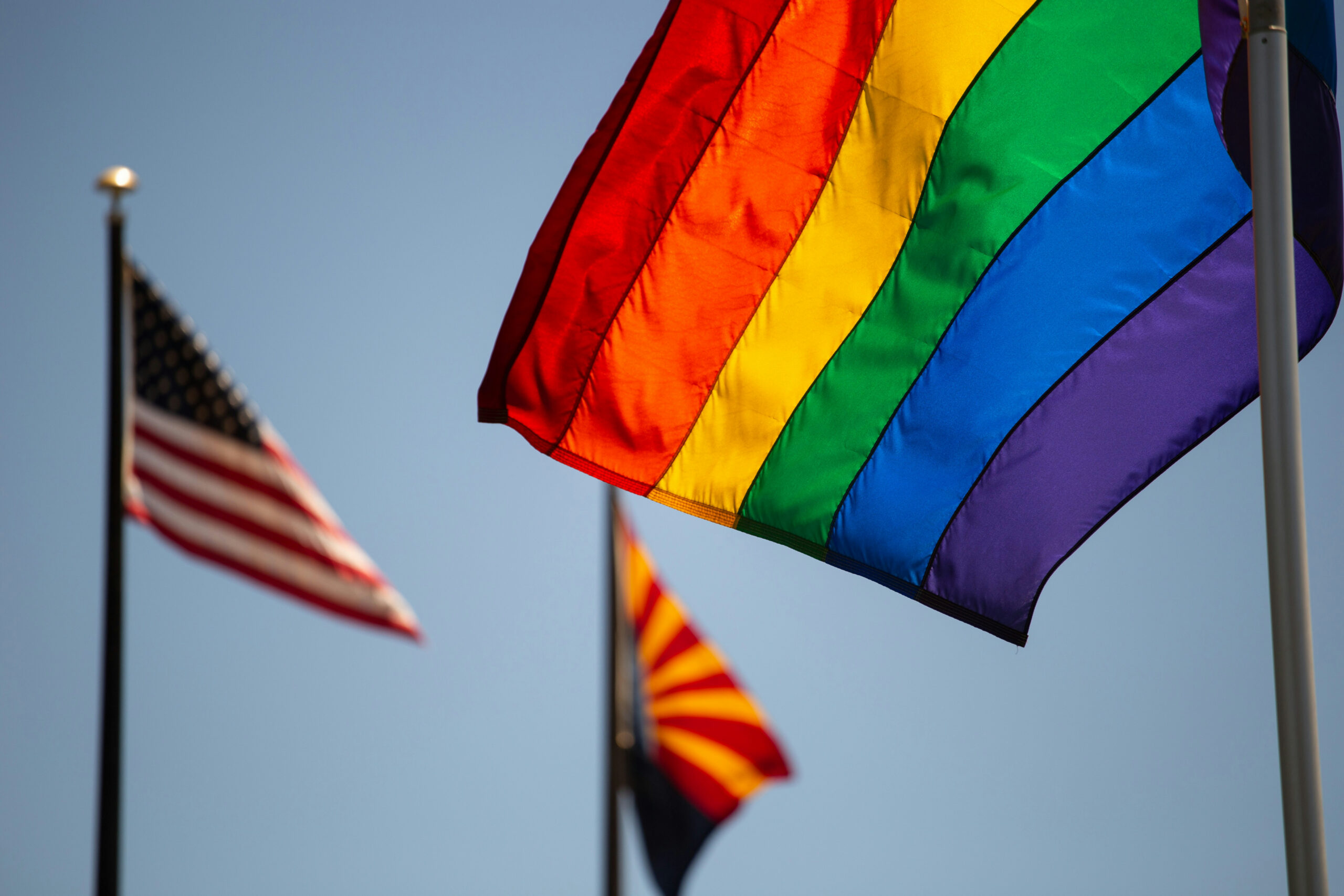 the pride flag flies in front of the American flag and Arizona state flag