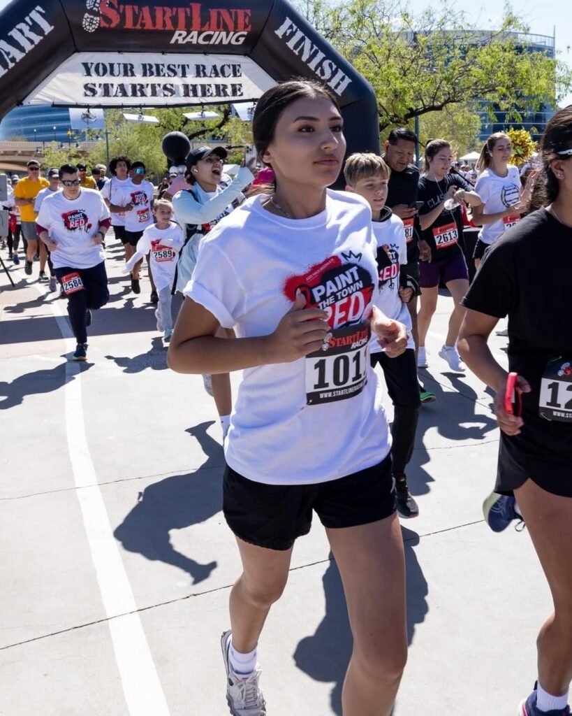 Runners start a race while a woman in a white shirt leads the pack.