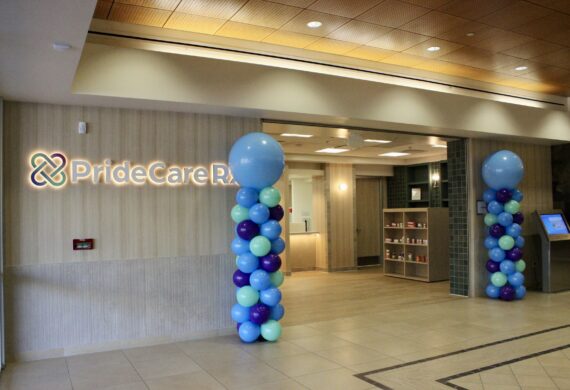 Hospital lobby entrance with wall signage reading PrideCare and balloon columns in blue, teal, and purple nearby.